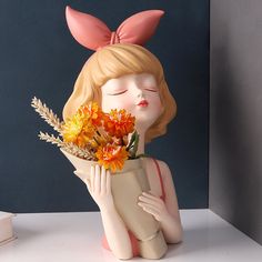 a ceramic figurine holding a vase with flowers in it's mouth and her eyes closed