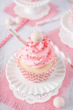 a cupcake with pink frosting and sprinkles on a white plate