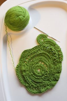 a green crochet doily and ball of yarn sitting on a white tray