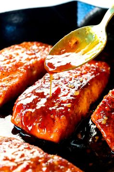 a spoon drizzling sauce onto some meat in a pan with other food items