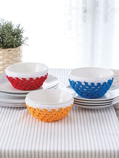 three bowls with crocheted designs on them sit on plates next to a potted plant