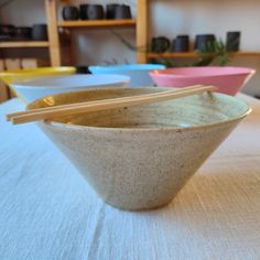 three bowls with chopsticks in them sitting on a white cloth covered tablecloth