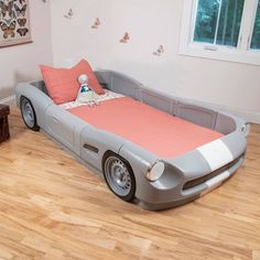 a child's car bed in the corner of a room with wooden floors and windows