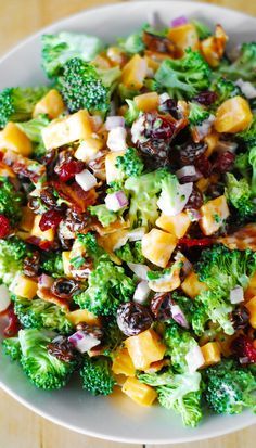 a white bowl filled with broccoli, cheese and cranberry salad on top of a wooden table