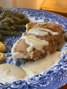 a blue and white plate topped with meat covered in gravy next to green beans