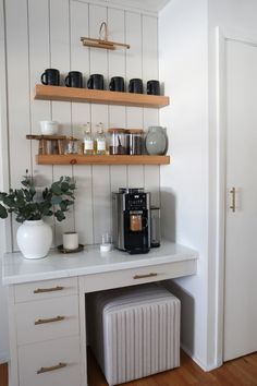 the coffee maker is sitting on top of the counter next to the shelf with cups and mugs