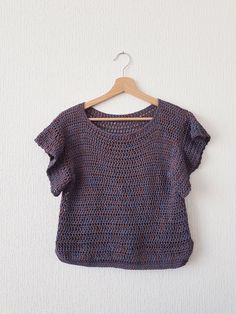 a knitted sweater hanging on a wooden hanger against a white wall with a wood hanger in front of it