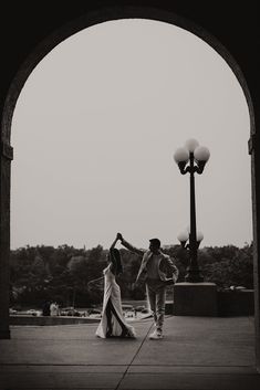 black and white photograph of two people dancing in front of a light pole with street lamps