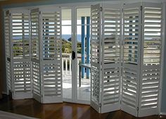 an open room with white shutters and wood flooring in front of a balcony