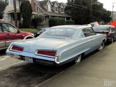 an old car is parked on the side of the road in front of other cars