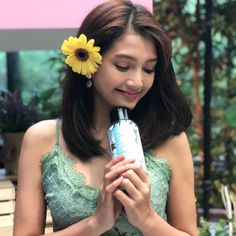 a woman in a green dress holding a blue and white water bottle with a yellow flower on her head