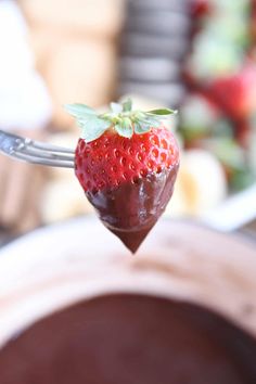 a strawberry on a fork with chocolate in the background