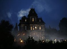 an old house lit up at night with fog in the foreground and trees around it