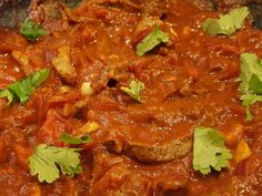 meat and vegetables are mixed together in a sauce with cilantro leaves on top