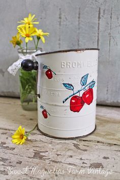 an old tin can with cherries painted on it and daisies in the background