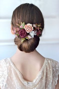 a woman with flowers in her hair is wearing a white dress and has an elegant bun hairstyle