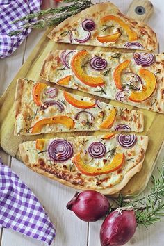 four pizzas with onions and peppers on a wooden cutting board next to garlic, onion, and herbs