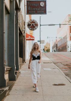 a woman is walking down the sidewalk in front of a sign that says fringe village