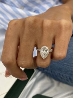 a close up of a person's hand wearing a ring with a pear shaped diamond