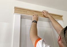 a man is working on the trim around a white door with wood planks in front of him