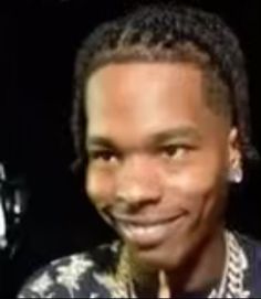 a man with dreadlocks smiles at the camera while standing in front of a black background