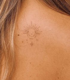 the back of a woman's neck with a small sun tattoo on it