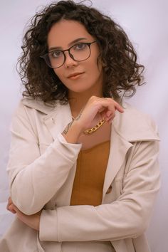 a woman wearing glasses and a jacket posing for the camera with her hand on her chin