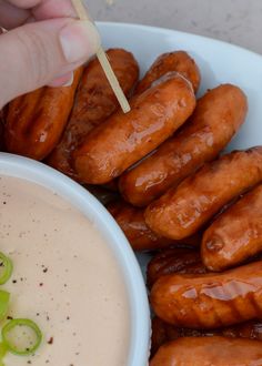 a person holding a toothpick over a bowl of hot dogs with dipping sauce