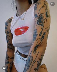 a woman with tattoos on her arm and chest wearing a white tank top that has red lips painted on it