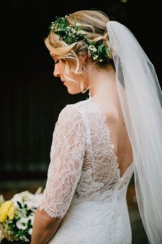 a woman in a wedding dress holding a bouquet and wearing a veil with flowers on her head