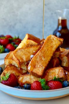 french toast with syrup being drizzled over berries and strawberries in a white bowl