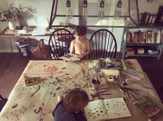 two young boys sitting at a table with books and paper work on the table top