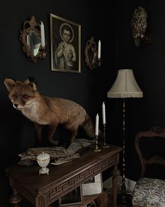 a fox standing on top of a wooden table next to a lamp and pictures above it