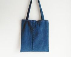 a denim tote bag hanging on a white wall with a black cord in it