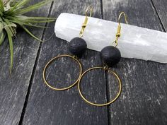 These hoop earrings feature 25mm raw brass open circle charms dangling beneath 12mm black lava stones.Lava is a very earthy stone, and has been said to give its wearers strength and courage, inspire stability through volatile times, and have calming properties that help to dissipate anger. These lava stone earrings can be used with your favorite aromatherapy oils or essential oils.HOW TO USE LAVA STONES WITH ESSENTIAL OILS:Its natural porosity makes lava stone a wonderful vessel for diffusing es Black Brass Hoop Earrings As Gift, Black Circle Earrings With Ear Wire, Black Circular Earrings With Ear Wire, Black Circle Hoop Earrings For Gifts, Lava Stone Jewelry, Black And Gold Earrings, Lava Jewelry, Stone Hoop Earrings, Beaded Jewelry Earrings