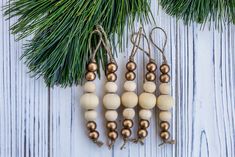 three wooden beads hanging from a christmas tree branch on a white wood background with pine needles