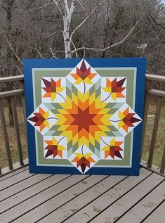 a colorful quilt sitting on top of a wooden deck next to a tree in the woods