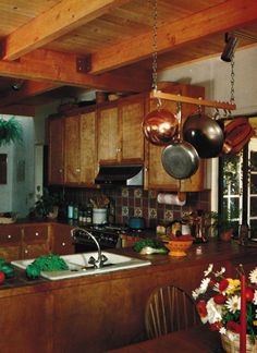 a kitchen filled with lots of wooden cabinets and hanging pots on the ceiling over an island