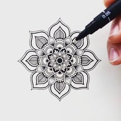 a person is holding a marker and drawing a flower with black ink on white paper