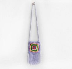 a crocheted bag hanging from a hook on a white wall with the handle down