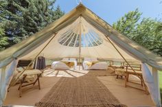 the inside of a large tent with two beds and chairs in it, outside on grass