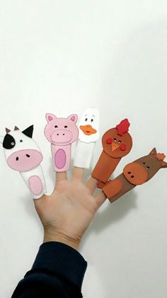 a hand holding five finger puppets with farm animals and pigs on them in front of a white wall