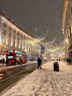 people are walking in the snow on a city street with christmas lights strung over it