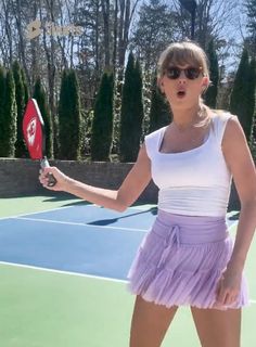 a woman holding a tennis racquet on top of a tennis court with trees in the background