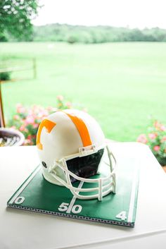 an orange and white football helmet sitting on top of a green mat in front of a field