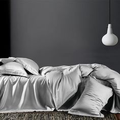 an unmade bed with white sheets and pillows in a dark room next to a lamp