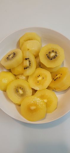 sliced kiwi fruit in a white bowl on top of a table with other fruits