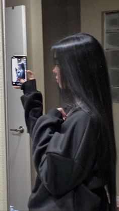 a woman taking a selfie with her cell phone in front of the door while wearing a black hoodie