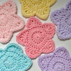 crocheted flowers are arranged on a white surface with blue, pink, yellow and purple colors