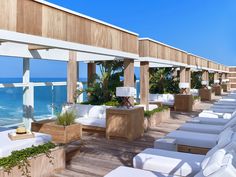 an outdoor lounge area overlooking the ocean with white chairs and plants on each side, along with large windows that look out onto the beach